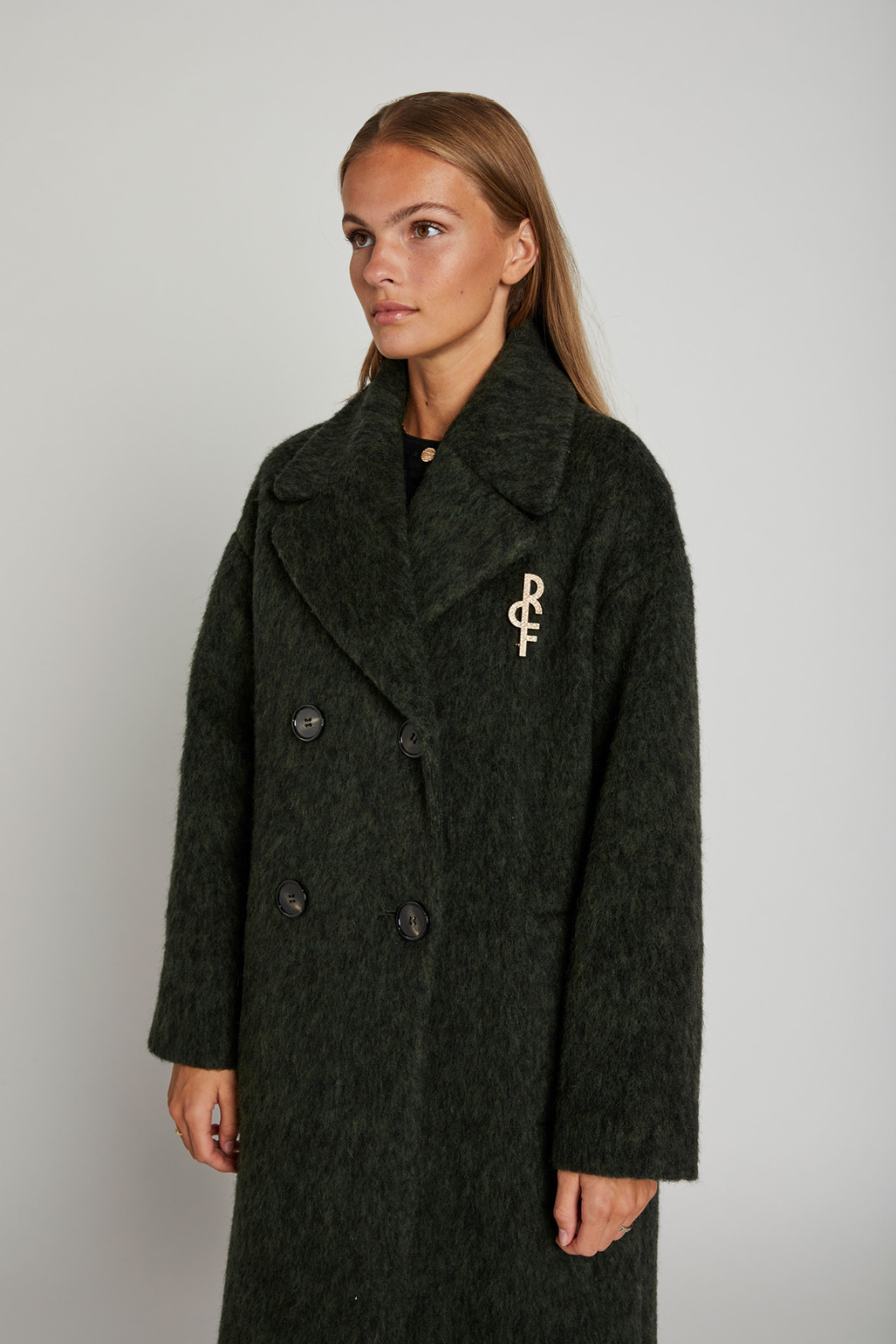 Jakke, frakke, coat, lang, grøn, army, mørk, uld, wool, uldjakke, broche, logo, varm, oversize, stor, dobbeltradet, ulden, lodden, langhåret, fin, smuk, elegant, klassisk, feminin, pæn, rå, cool, sej, unik, musthave, hverdag, fest,